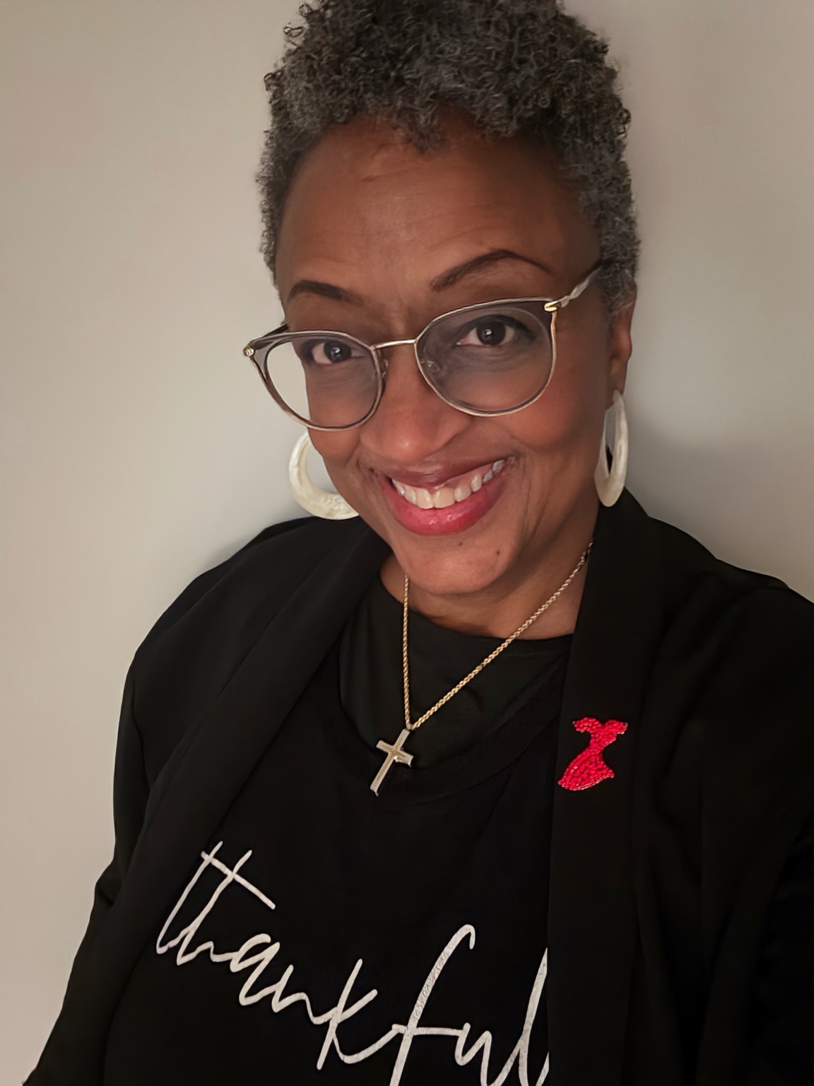 Debora Grandison smiling, wearing glasses and a black jacket with a red dress pin