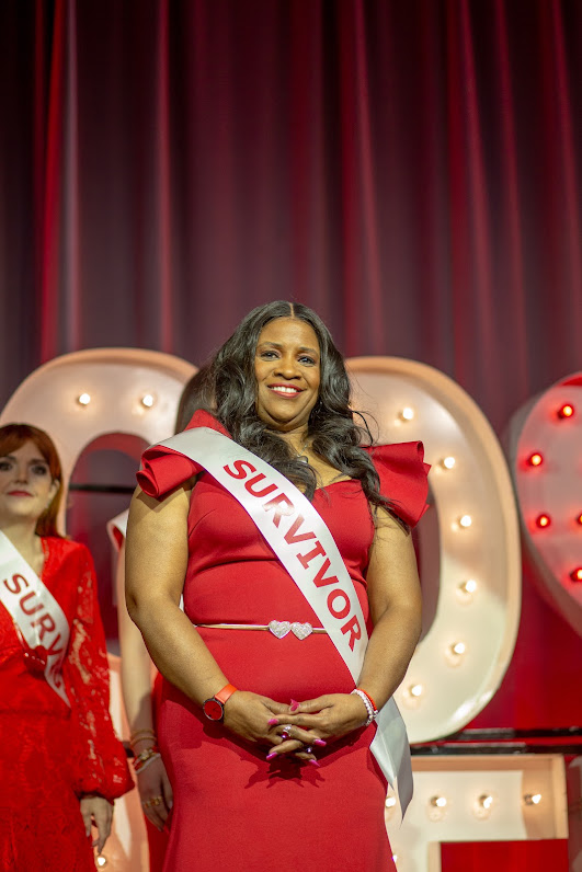 Sharon Bond smiling on stage in a red gown and Survivor sash